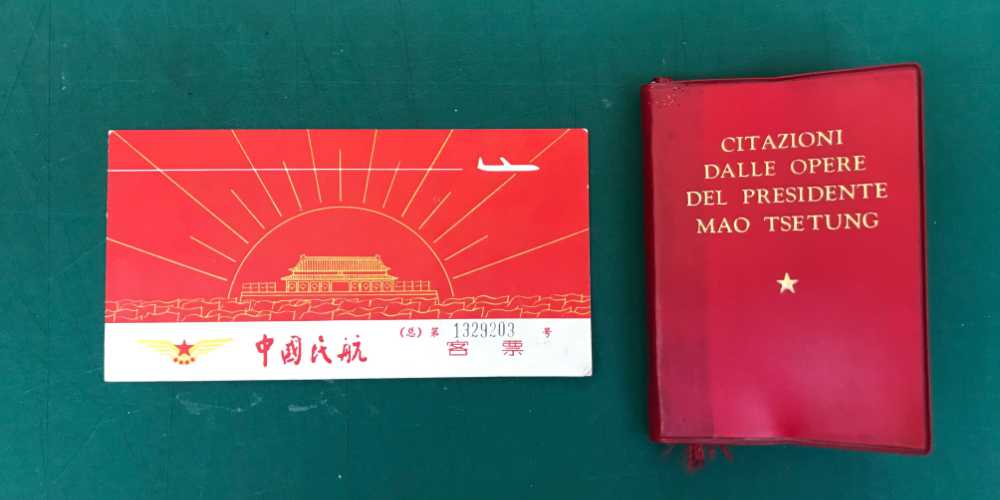 A vintage airline ticker with a chinese temple and stylised jet plane on the cover, next to it is a red book containing the teachings of Chairman Mao.