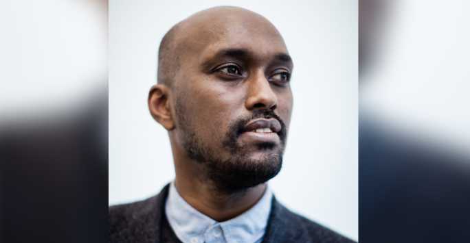 Young black male with shaven head, trimmed beard and buttoned up shirt.