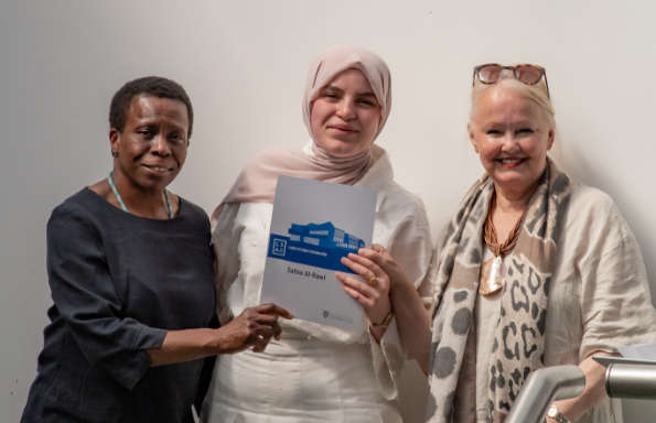 Three women standing in celebration, the middle one holding a certificate.