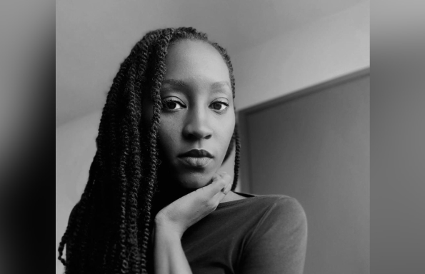 Young woman with long braided hair looking towards the camera with her chin resting on her left hand.
