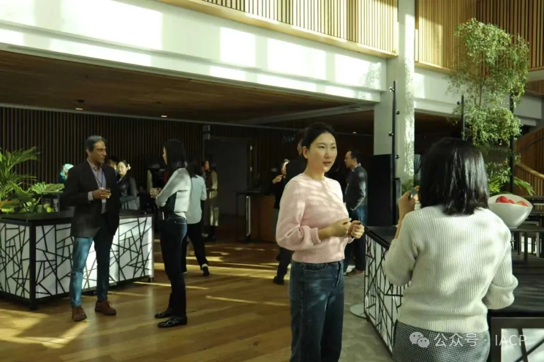 In an atrium two smartly dressed women are having a discussion, behind them a man and a women are talking.