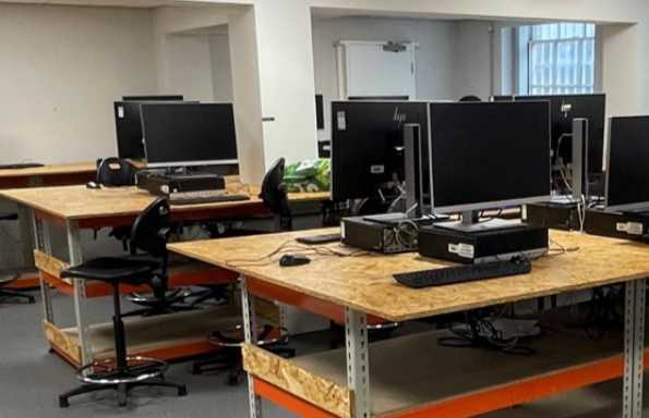 Metal framed wooden tables with computers, monitors and keyboards on top.