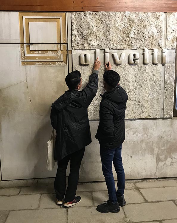Two students examining a stone Olivetti logo