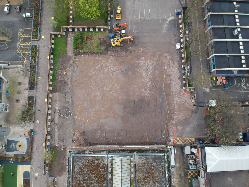 Aerial view of a building site with the outline of a new building drawn on empty ground. two mechanical diggers are parked at the top.
