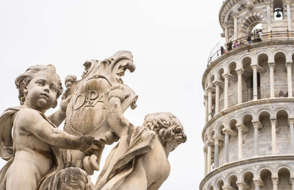 In the foreground two stone carved cherubs hold a stone carved, behind them the leaning tower of Pisa is partly visible.