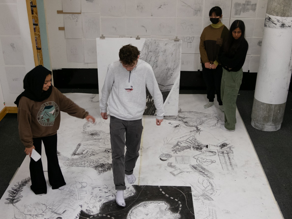 An asian woman directs an asian man on a giant paper map with an architectural scheme drawn on it in charcoal