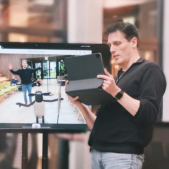 Man holding tablet computer in front of screen showing Augmented Reality scene with Shawn the Sheep