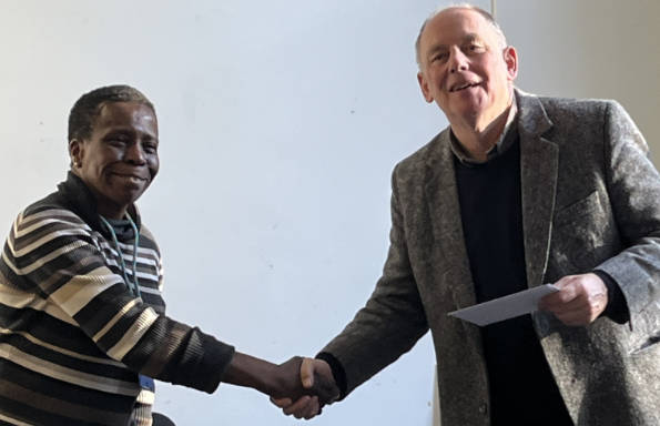 A woman shaking hands with a man having presented him with a leaving card on his retirement.