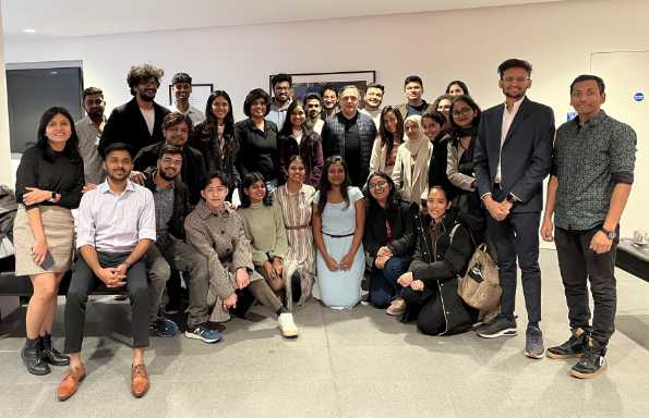 Inside a lecture room, two rows of staff and students smiling for the camera at the spring forum.