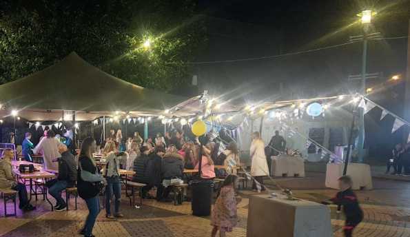 A lively evening gathering of people under a sail based awning.