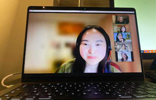 A Laptop screen showing a zoom call taking place. A woman is speaking, with thumbnails of the other participants down the side.