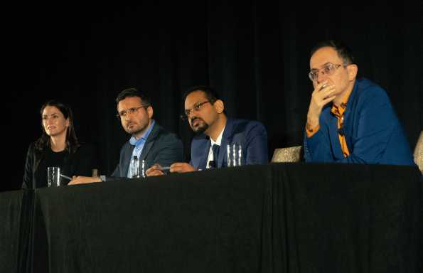 A woman and three men sitting at a table looking out towards an audience. All look as though they are listening to a question being asked.