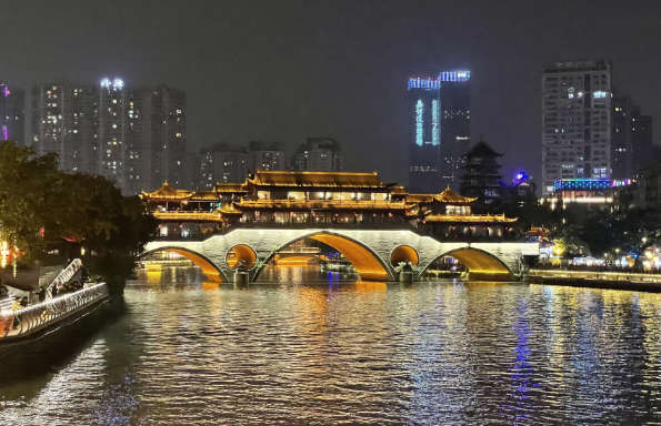 A Chinese river by night, a bridge is illuminated, a modern city is visible behind.