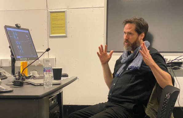 Middle aged bearded white man sitting in front of a computer gesticulating.