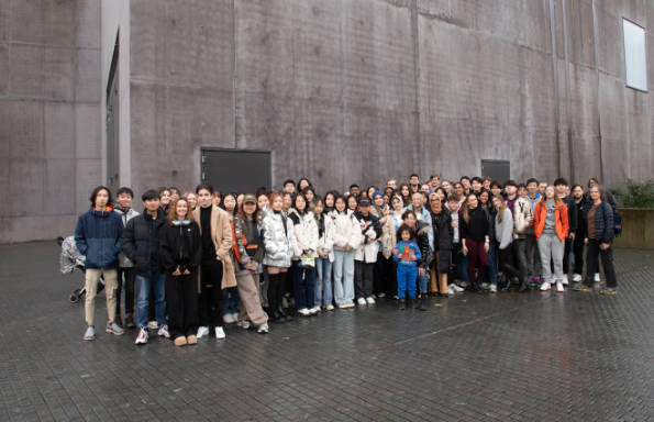 large group of students and staff lined up in front of a concrete wall outside an art gallery.