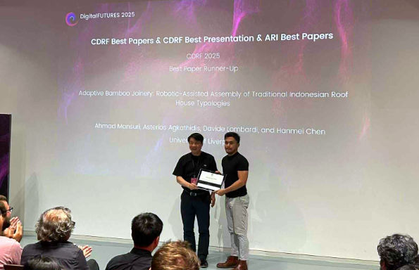 Two men standing on a stage, one presenting the other with a certificate and shaking his hand.