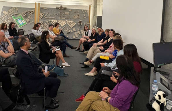 A panel of seated men and women discussing with an audience. TO the side of them is a large vertically mounted site model of Liverpool's China Town.