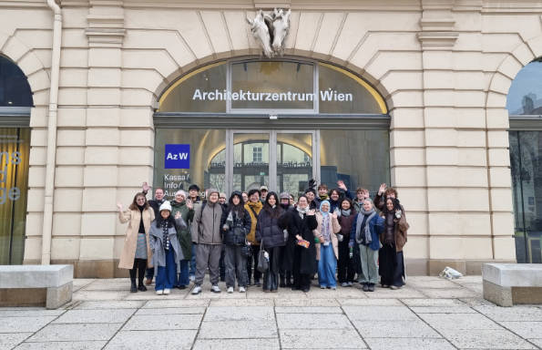 A group of students and staff standing outside a large glass frontage set into a stone arch.