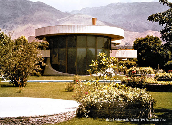 Circular house with flat concrete roof, set in garden with Iranian mountains in the background