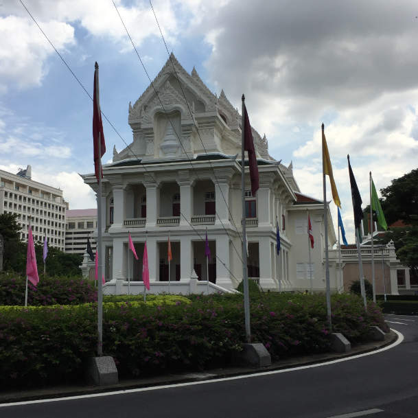 A two storey white concrete building with tall pointed roofs with elaborated ornaments. The roof consisted of multiple layers in both directions. On both floor there are external corridors. There is also a stupa relief above the second floor.