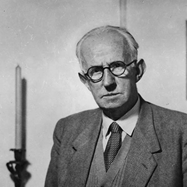 Older man wearing a tweed suit, waistcoat and tie, sitting beside a candlestick in © University of Liverpool Special Collections and Archives.