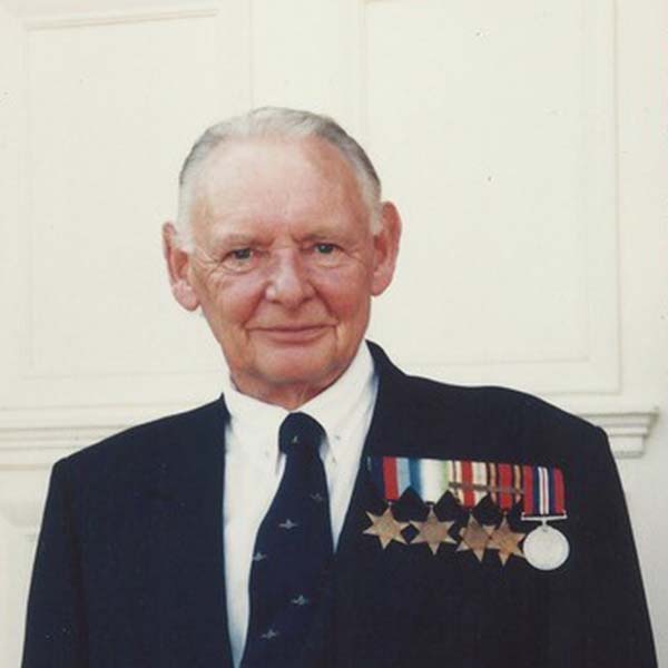 Retired man standing in front of a door wearing a blue jacket with medals