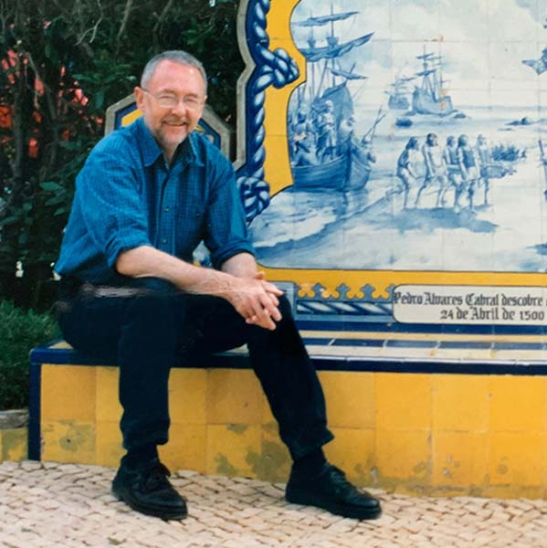 Middle aged man with grey hair and beard sitting in front of a ceramic fresco