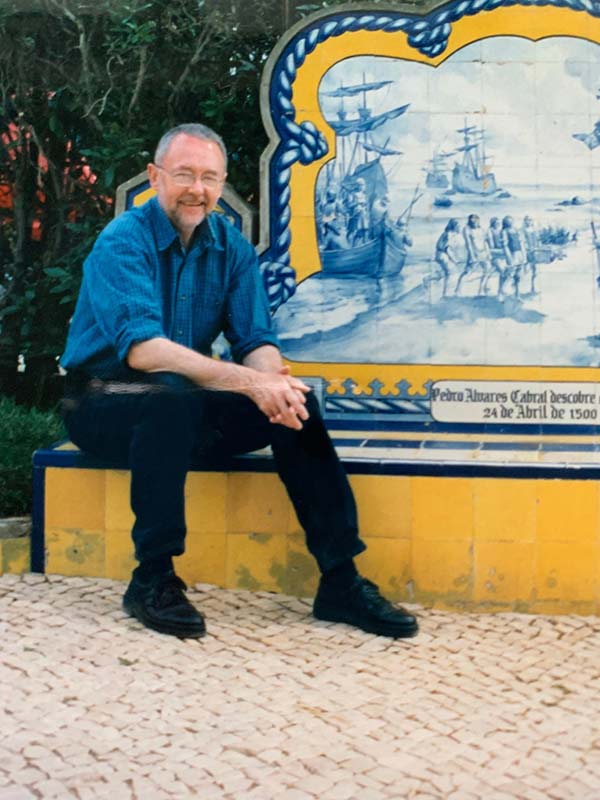 Middle aged man with grey hair and beard sitting in front of a ceramic fresco