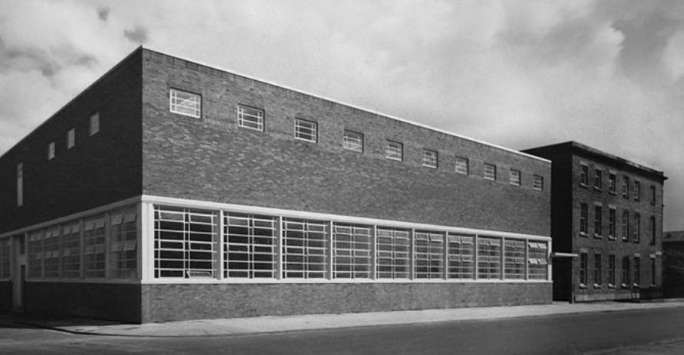 1930's brick building with large concrete framed windows on the lower floor and smaller metal framed ones on the second. A Georgian building is visible to its right.