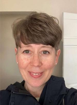 Smiling middle aged woman with short cropped hair and wearing a heavy black outdoor fleece jacket.