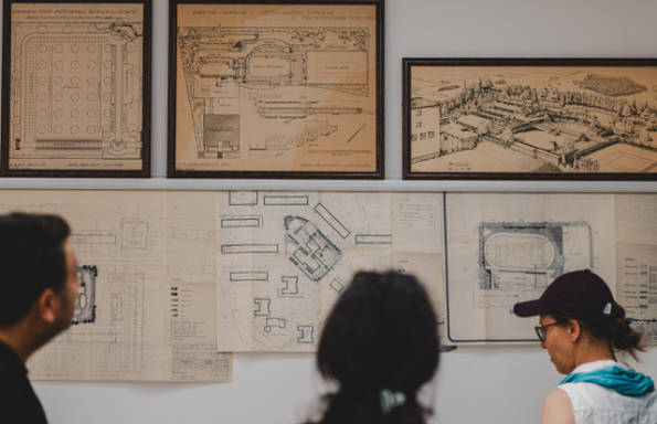 A man and two women standing and looking at old landscaping plans pinned to a wall.