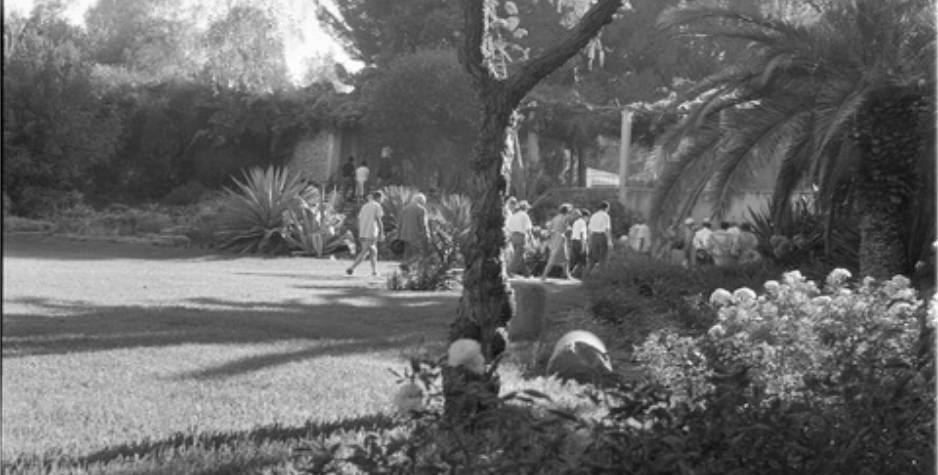 A vintage photograph of a landscaped garden, in the distance can be seen a group of men and women.