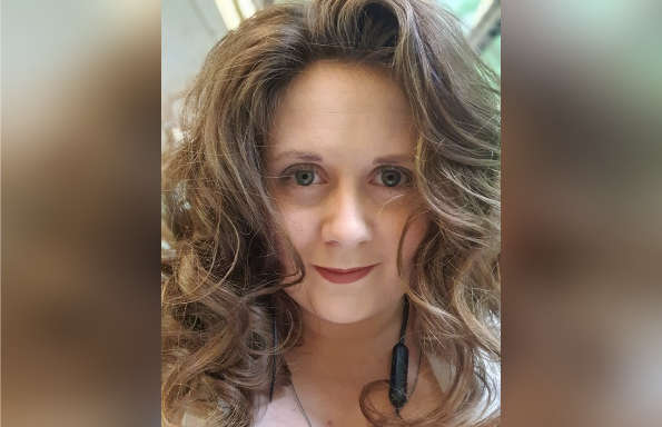 Woman smiling at the camera. She has long big hair and is wearing earphones.