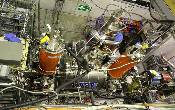 The horizontal Penning trap magnet and orange cryostats form part of the BASE experiment.