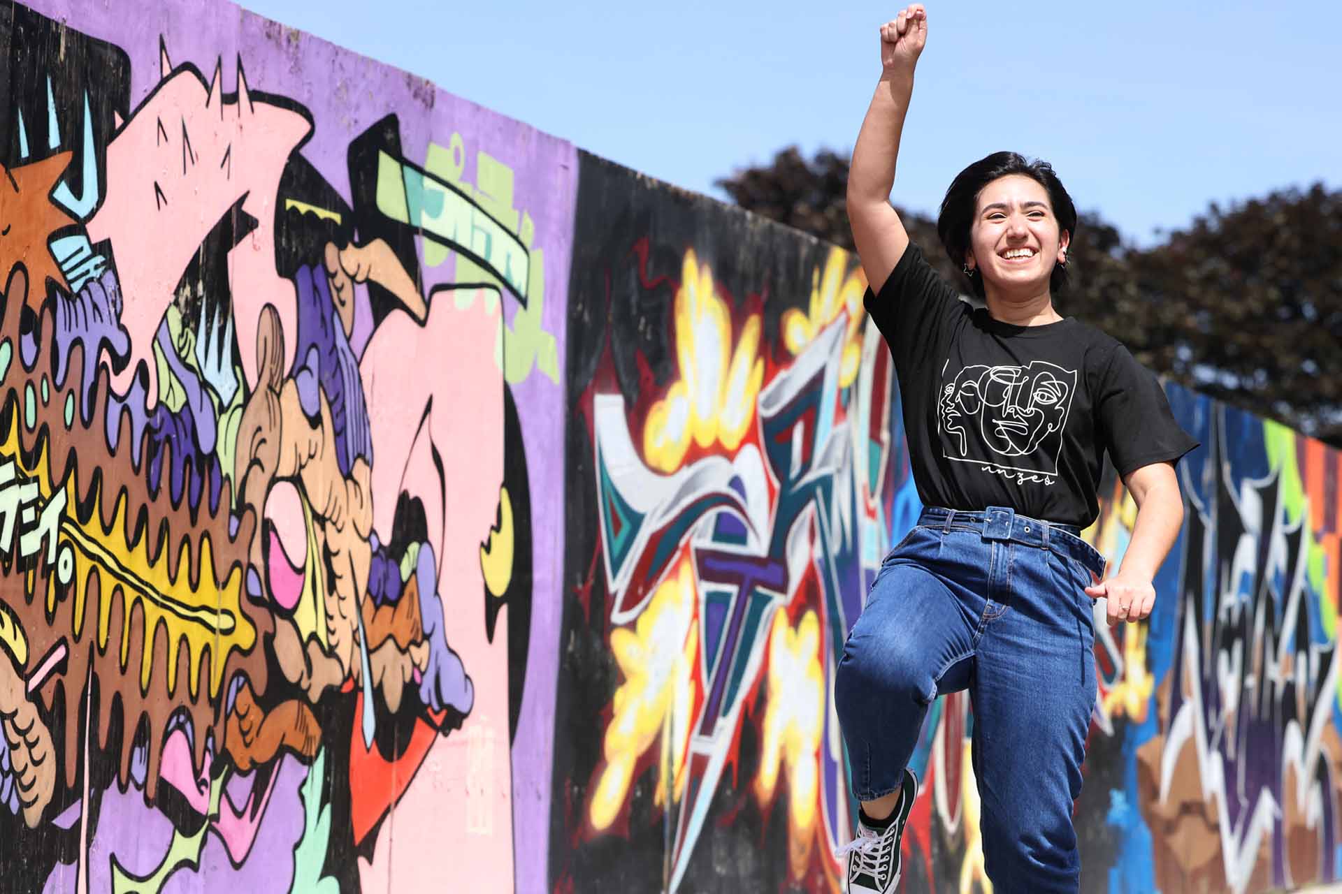Student jumping in the air in front of a colourful painted wall