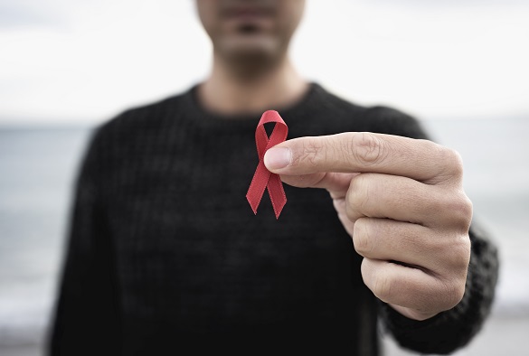 A person holds a red AIDS awareness ribbon out to the camera