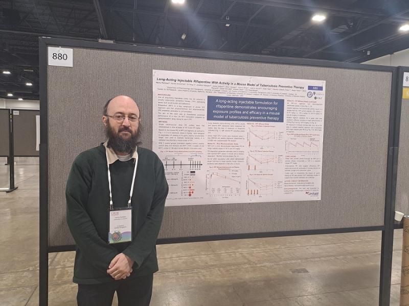 Henry is stood in front of the poster he presented at CROI 2024. Henry is looking into the camers with his arms relaxed in front of him.