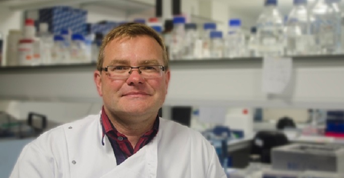 Dr James Stewart is stood in his lab looking into the camera
