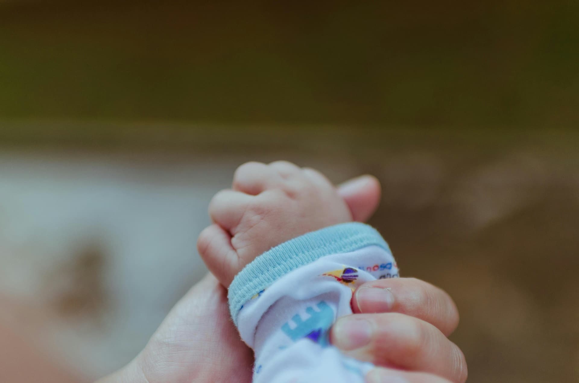 A baby's hand is gripping the thumb of the adult holding it.