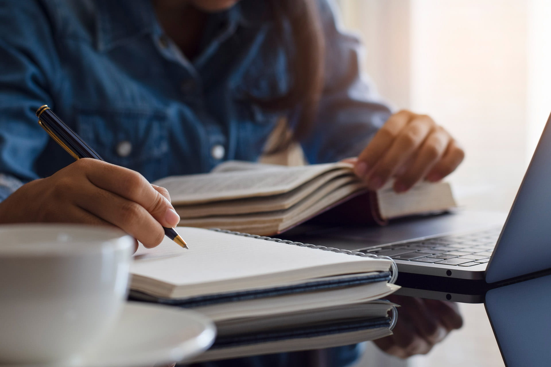 Close up of person looking in a book while writing in a notebook