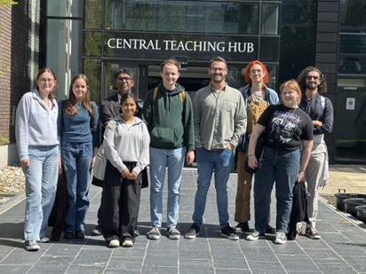 A diverse group of people stands outside the central teaching hub, engaged in conversation and enjoying the sunny day.