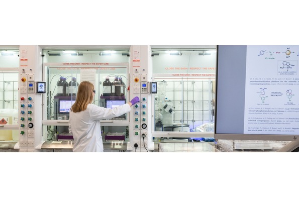 A woman in a lab coat is focused on her work while using a computer in a laboratory setting.