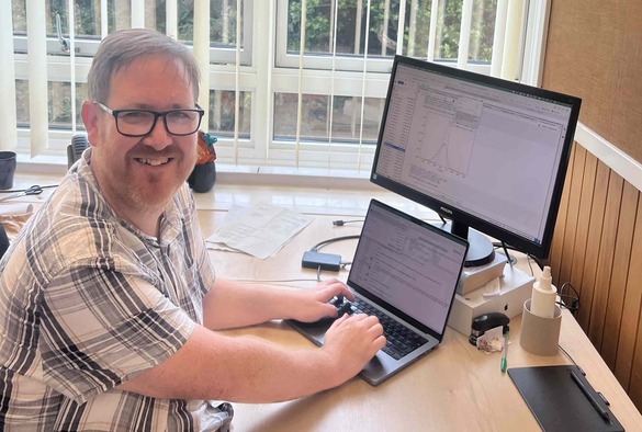 carl gwilliam sitting at his desk on laptop with a monitor behind it