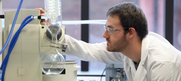 man wearing goggles in white lab coat using a machine in a lab enviroment