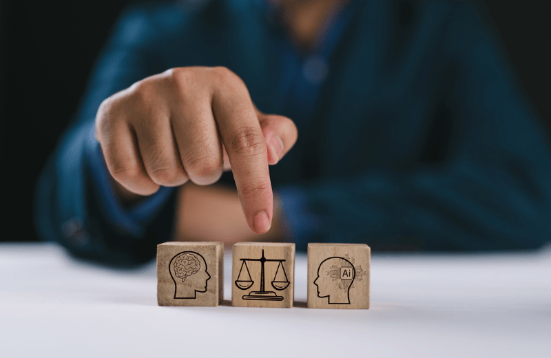 Three wooden blocks on a table, with icons on then symbolising the transfer of knowledge between an AI system and a human in the legal sector