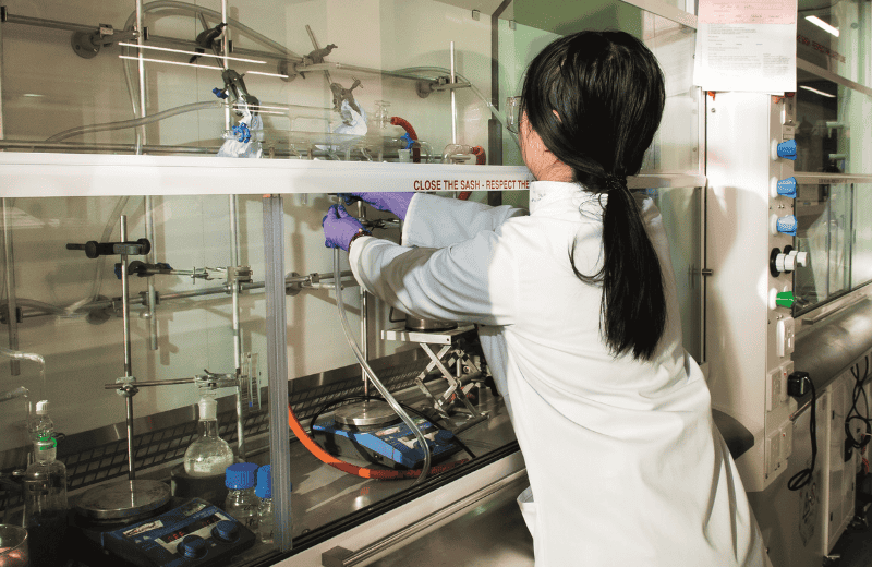 Scientist working in chemisty lab wearing white lab coat and saftey goggles