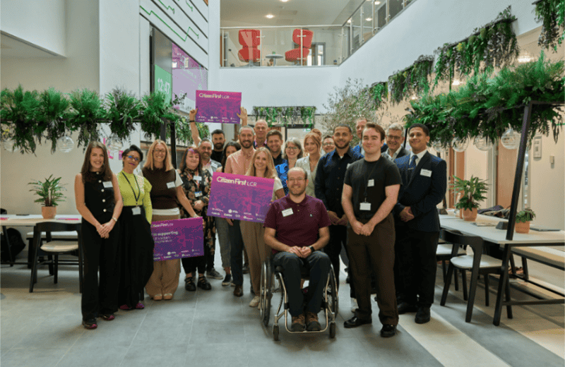A group on entrepreneurs standing in an atrium, holding cards that read Citizens First LCR