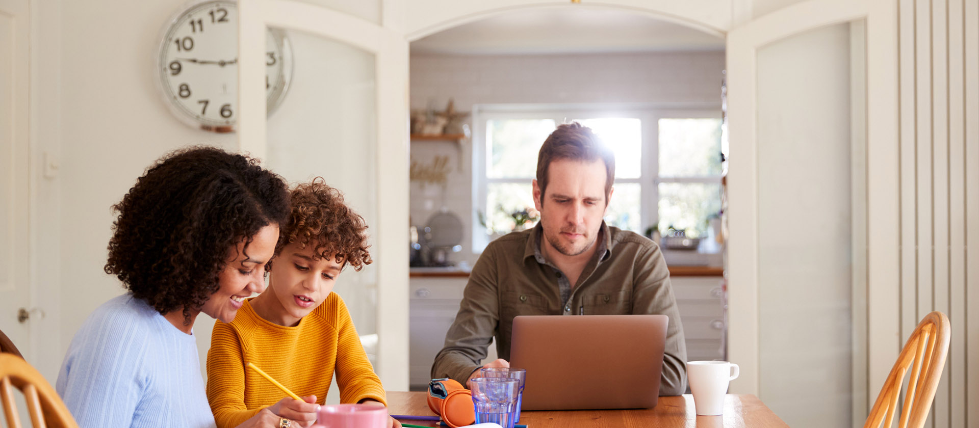 Family sitting at table with father working on laptop