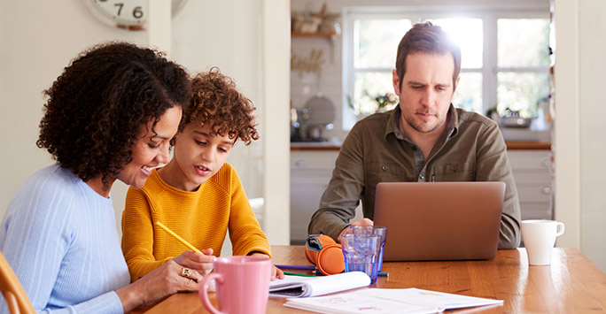 Family sitting at table with father working on laptop