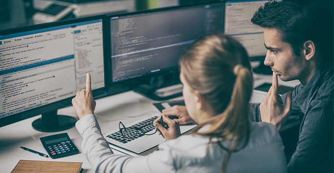 Man and a woman looking at code on computer screens